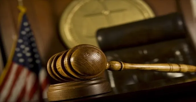A judge's gavel on a courtroom bench in front of an American flag